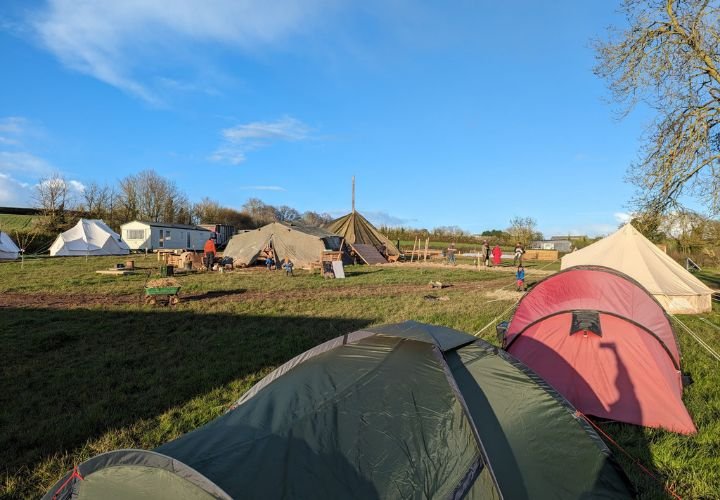 Several tents pitched in an open field at One Tree Farm, with people involved in sustainable activities.